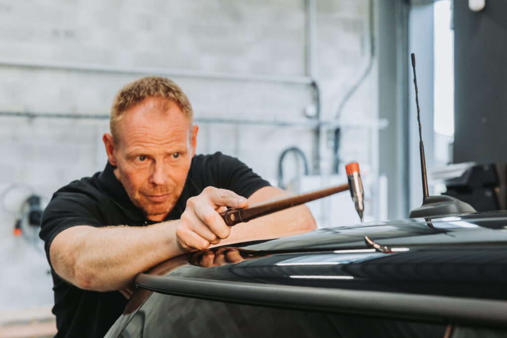 Technicien de la Carrosserie DEVINAST réalisant un débosselage sans peinture à Brognard